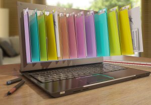 A laptop with folders representing digital files bursting out of the screen in a home office setting.