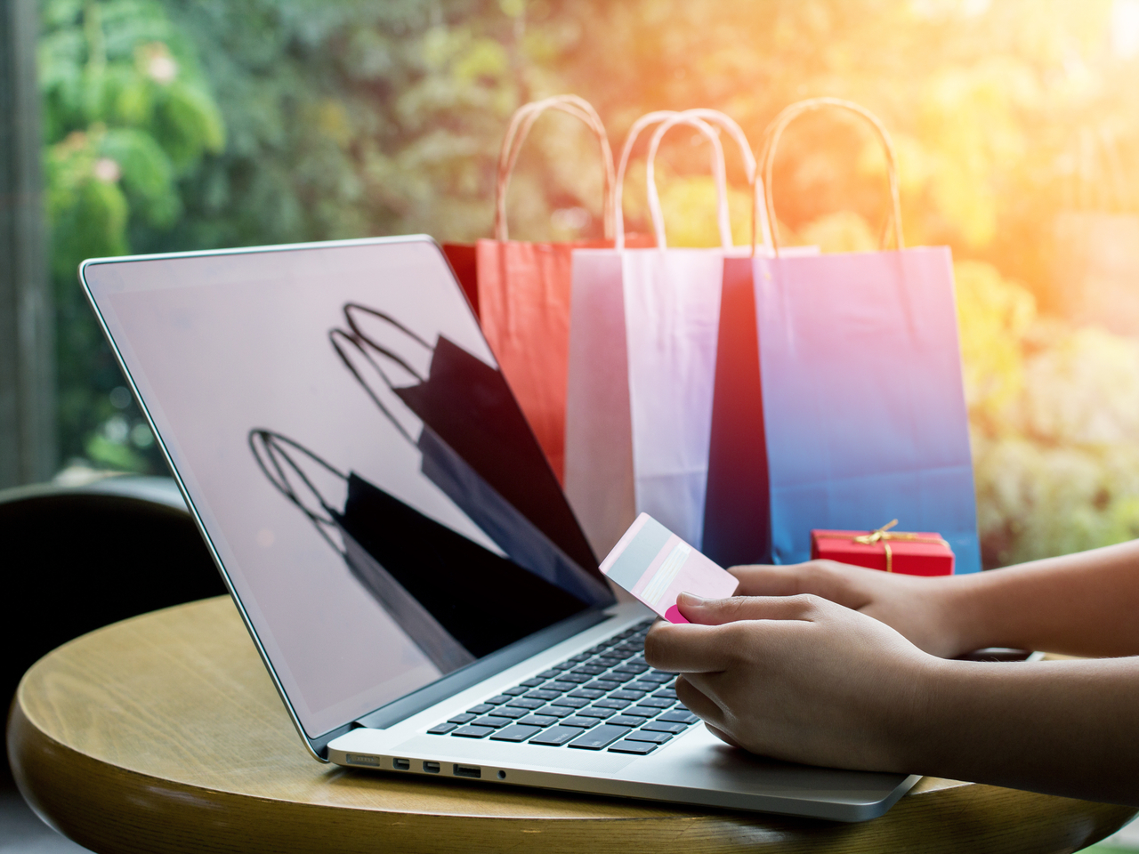A person holding a credit card and shopping online on a laptop with shopping bags in the background.