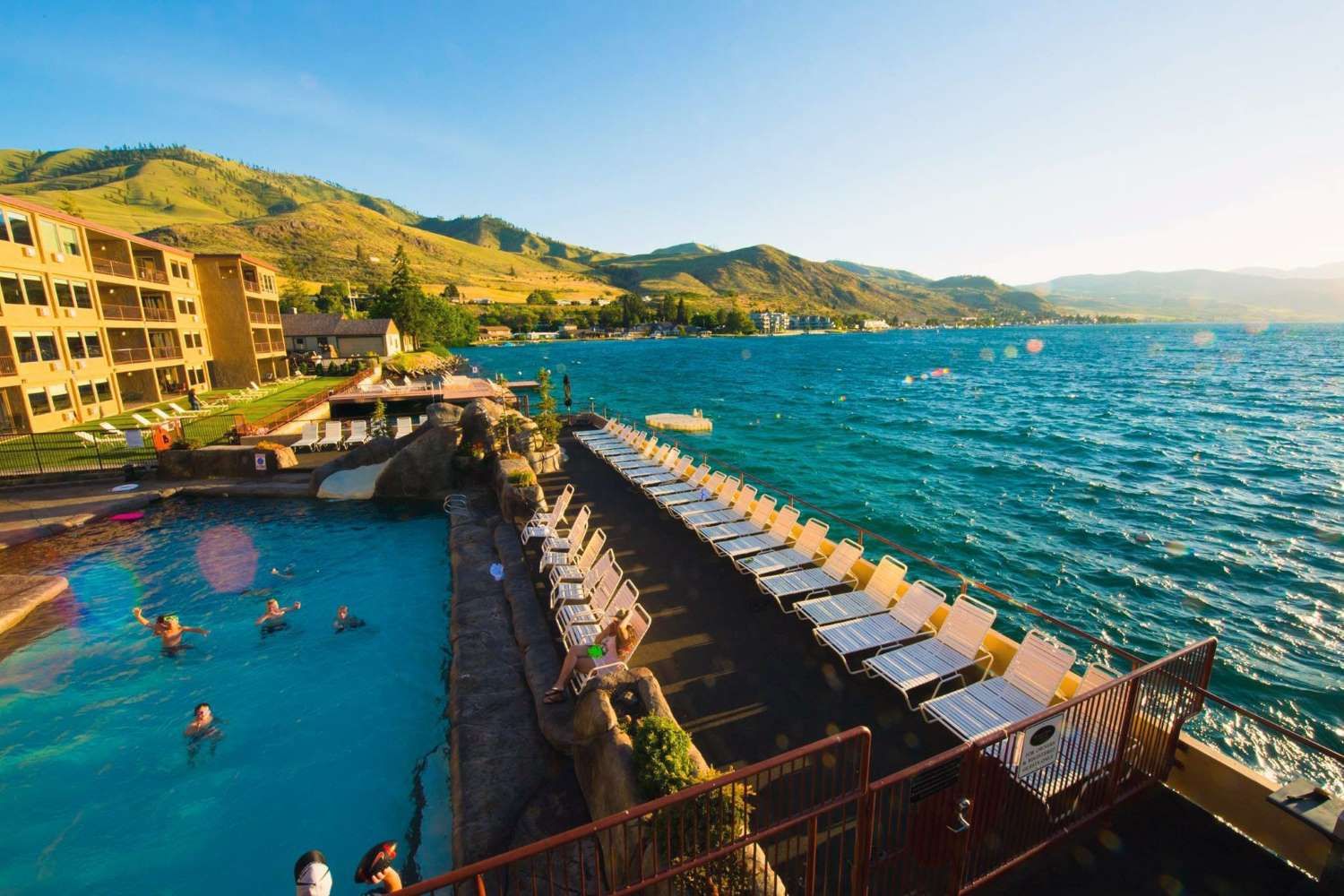 A lakeside resort with a pool and lounge chairs with a mountainous backdrop representing budget-friendly vacation destinations with low travel and accommodation costs.