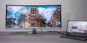 Laptop with an ultrawide curved monitor on a desk, showing a cityscape with trees and buildings.