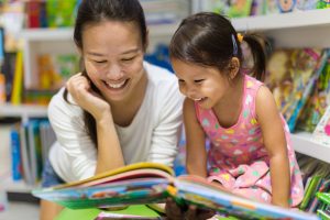 A mother and her daughter are sitting in a bookstore, looking at a book together.