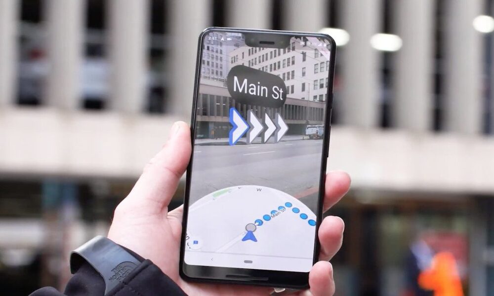 A hand holding a smartphone with the Google Maps app open and directions displayed on the screen with 'Main St' in the center.
