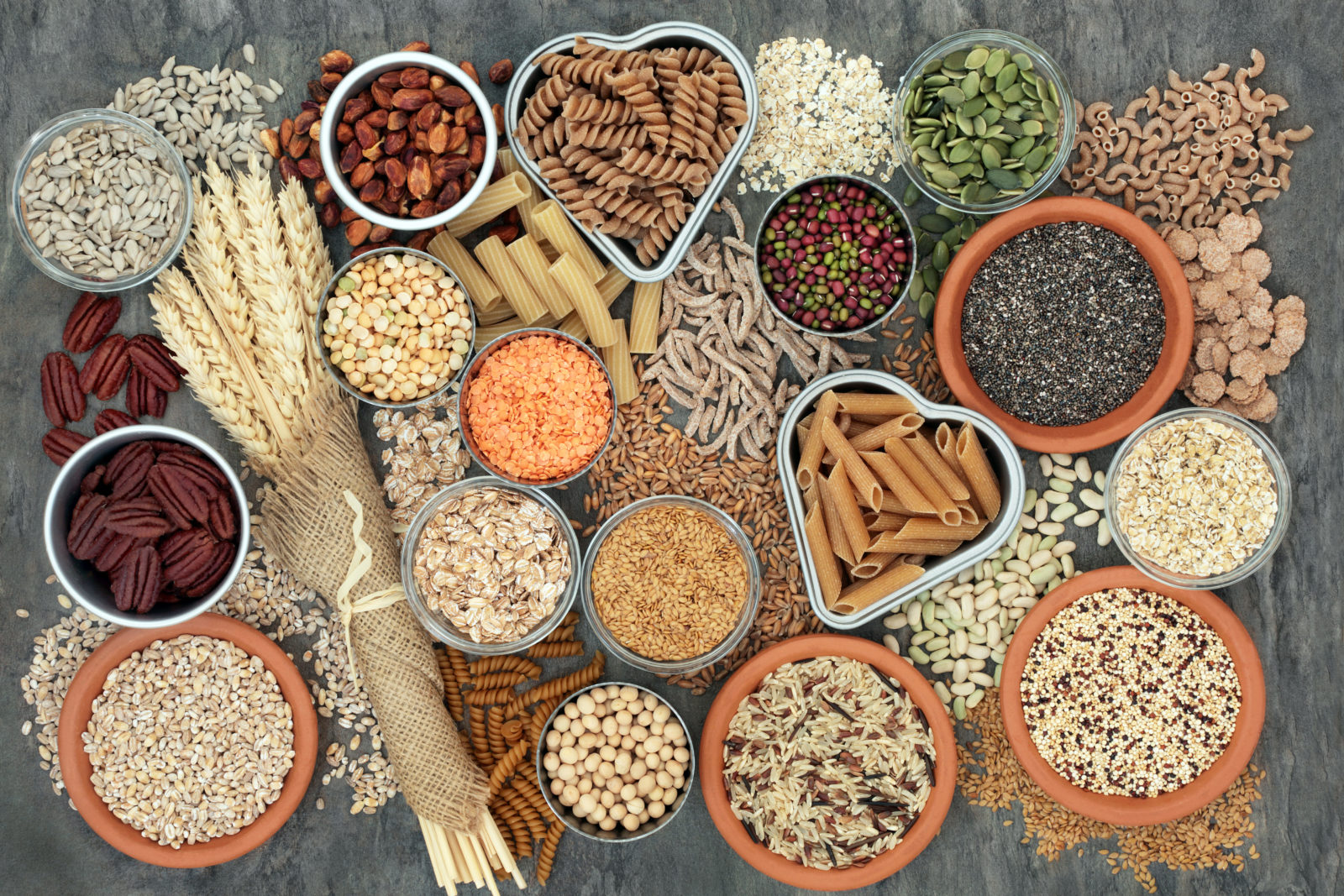 A variety of grains, seeds, nuts, and legumes are arranged on a slate background.