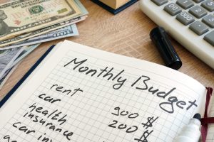 Image of a notebook with a list of monthly expenses and a calculator on a wooden table.