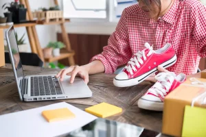 A woman is using a laptop to sell shoes online.