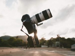 A close-up of a camera lens pointed up toward the sky with a strap hanging down, representing the search query 'Tips to sell photos on Shutterstock'.