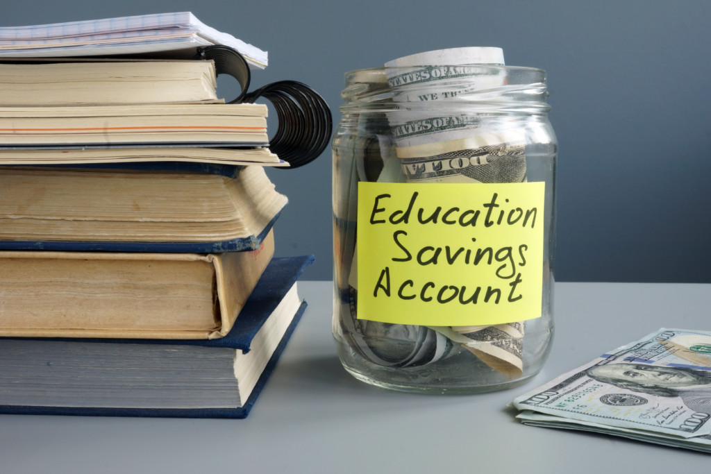 A jar labeled 'Education Savings Account' sits in front of a stack of books representing an app with a feature for auto-investing in a child's education savings account.