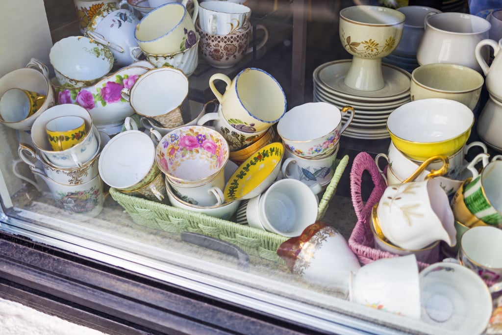 A variety of used and vintage teacups and saucers are displayed in a window.