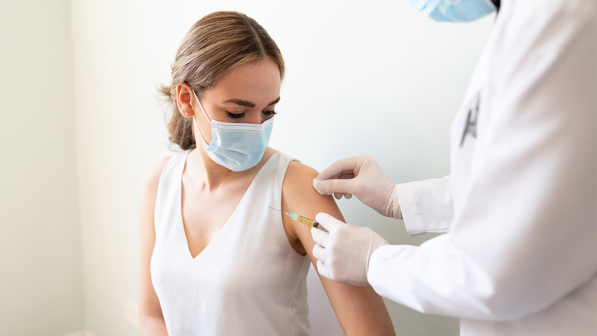 A young woman wearing a mask getting vaccinated by a doctor in a white coat and gloves. (Vaccination protects the community by preventing the spread of disease.)