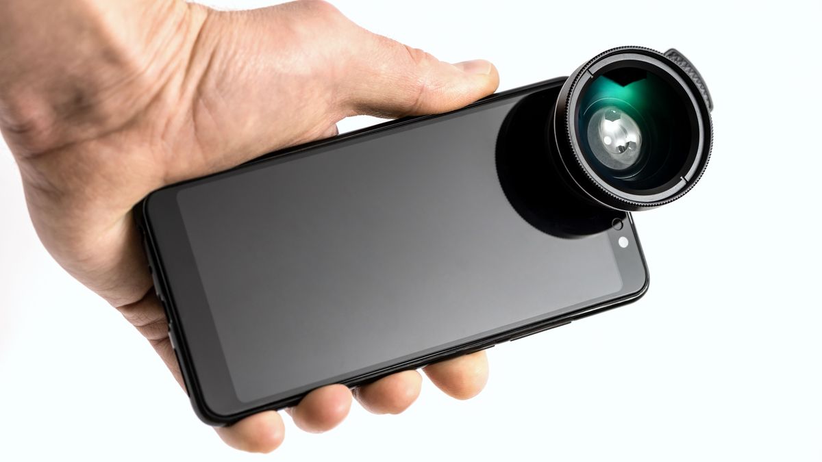 A hand holding a smartphone with a camera lens attachment.