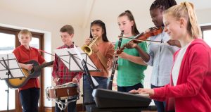 A group of students play various musical instruments in a classroom.