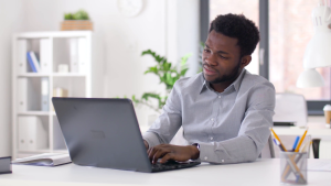 A man in a blue shirt is using a laptop computer to manage an online advertising campaign.