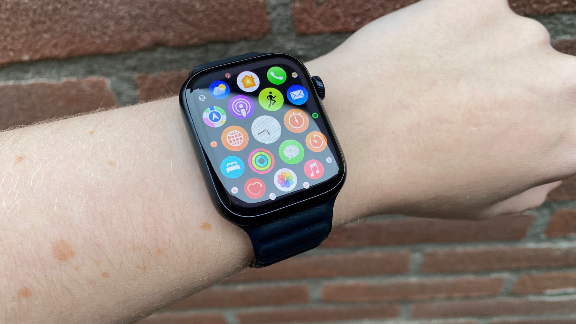 A person wearing an Apple Watch with the screen on and displaying the watch face with the installed apps including WhatsApp.