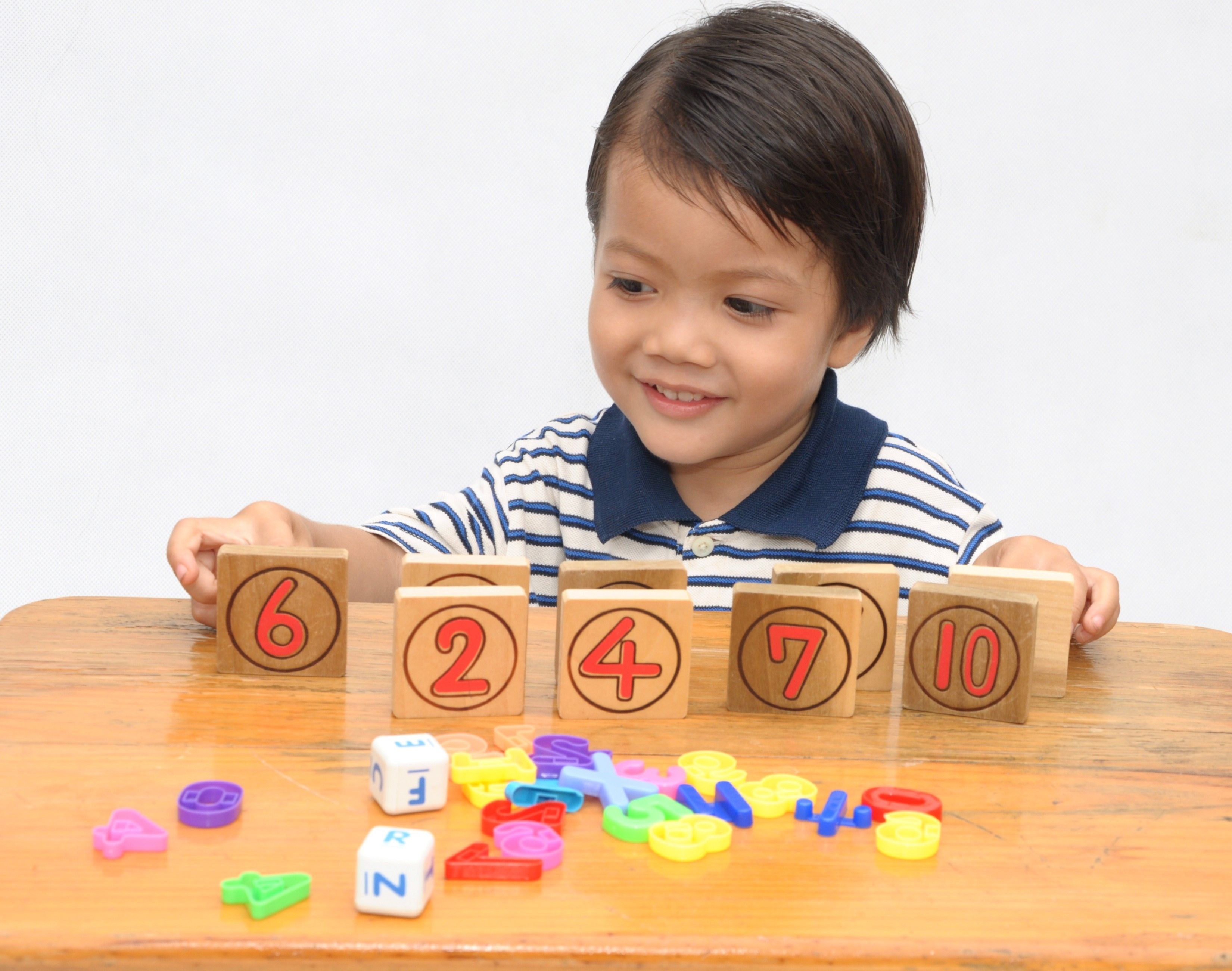 A young boy is learning numbers with colorful wooden blocks and plastic toys.