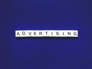 A blue background with white tiles spelling out 'ADVERTISING'. The image represents the search query 'Apps that make money without inviting friends'.