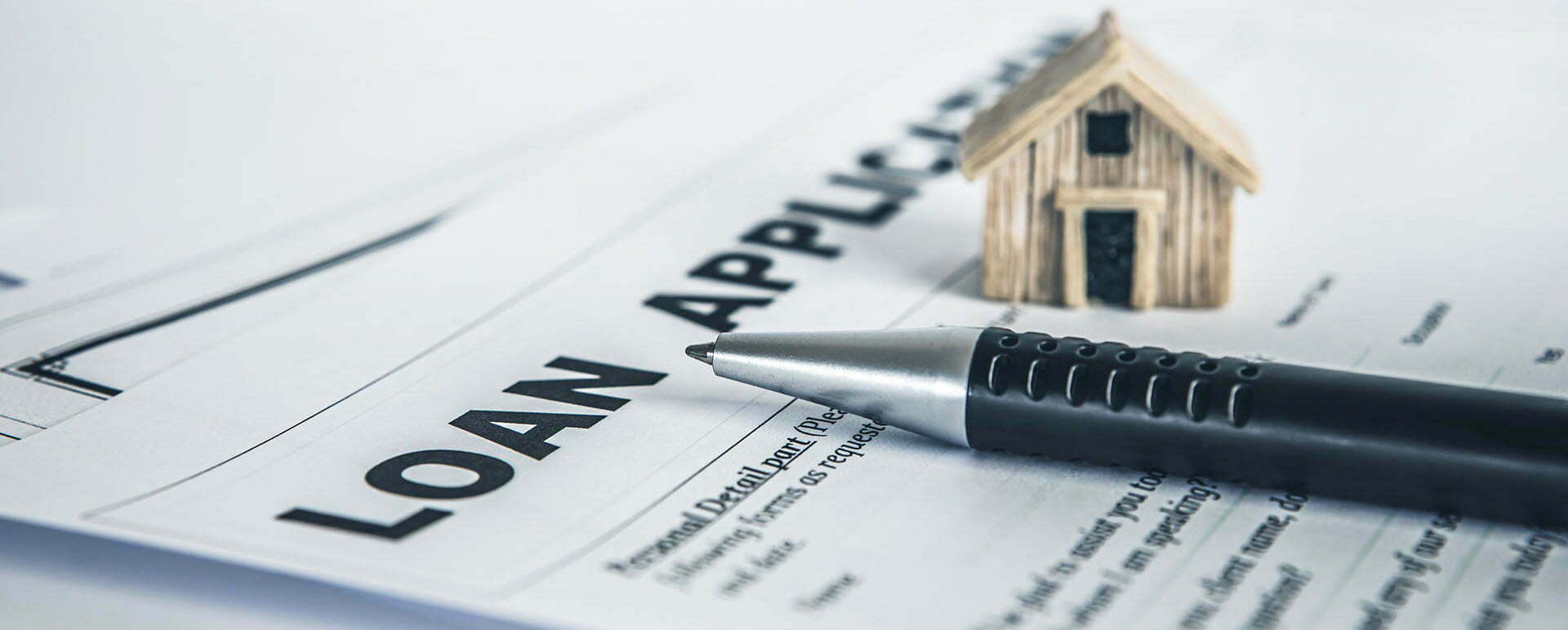 A pen resting on a loan application form with a miniature house sitting beside it.