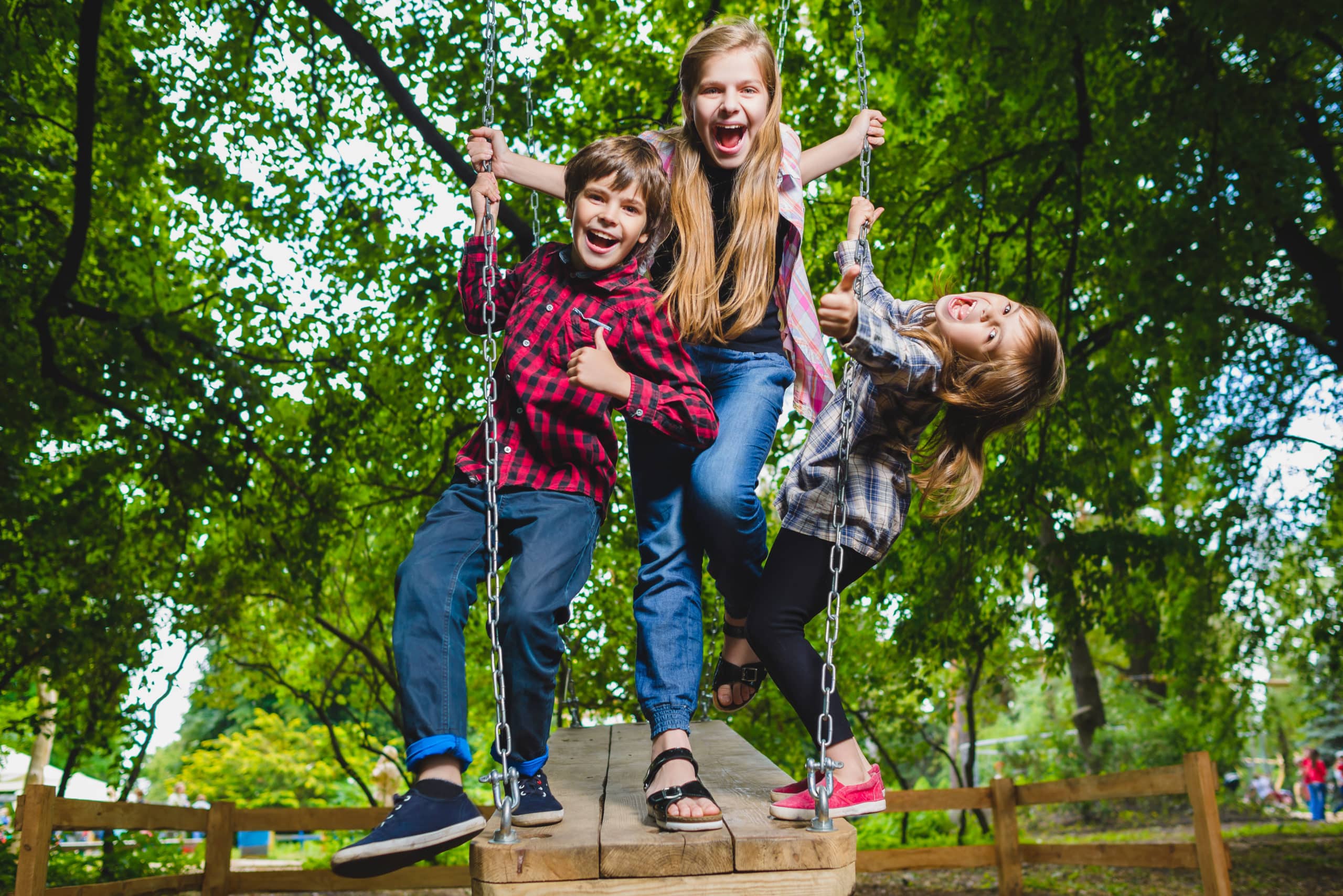 Three happy children are playing on a swing set in a park.