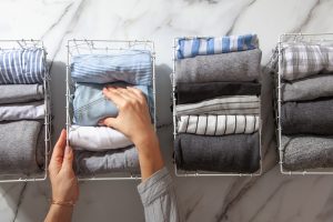 A person is folding and organizing clothes into wire baskets labeled with different categories.