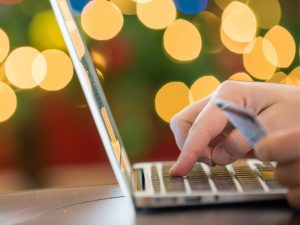 A person using a laptop to shop online with a Christmas tree in the background.