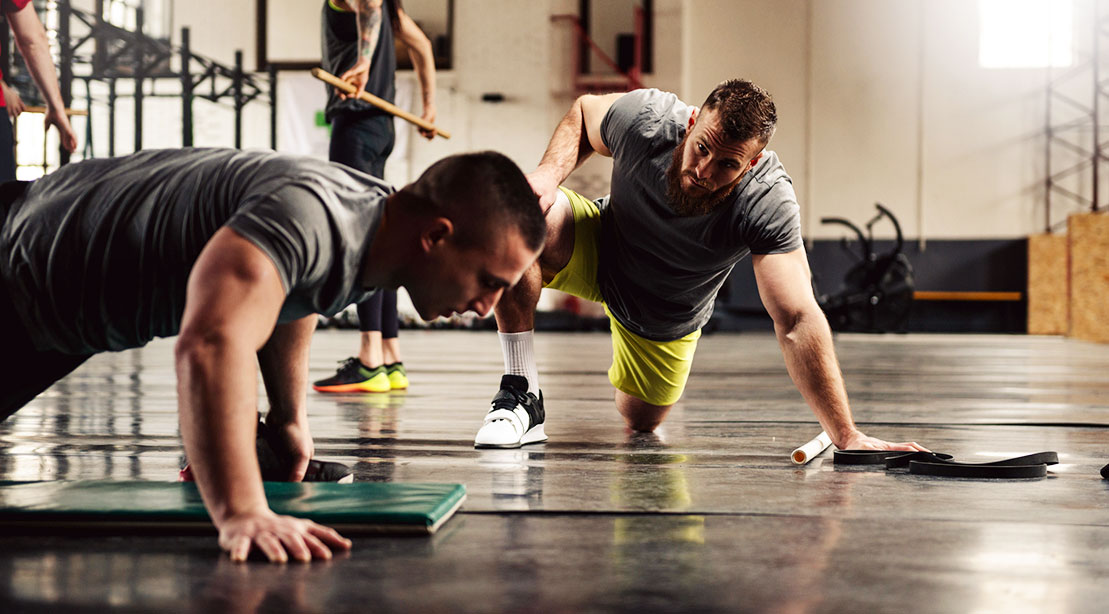 A personal trainer is helping a client with his push-ups in a gym.