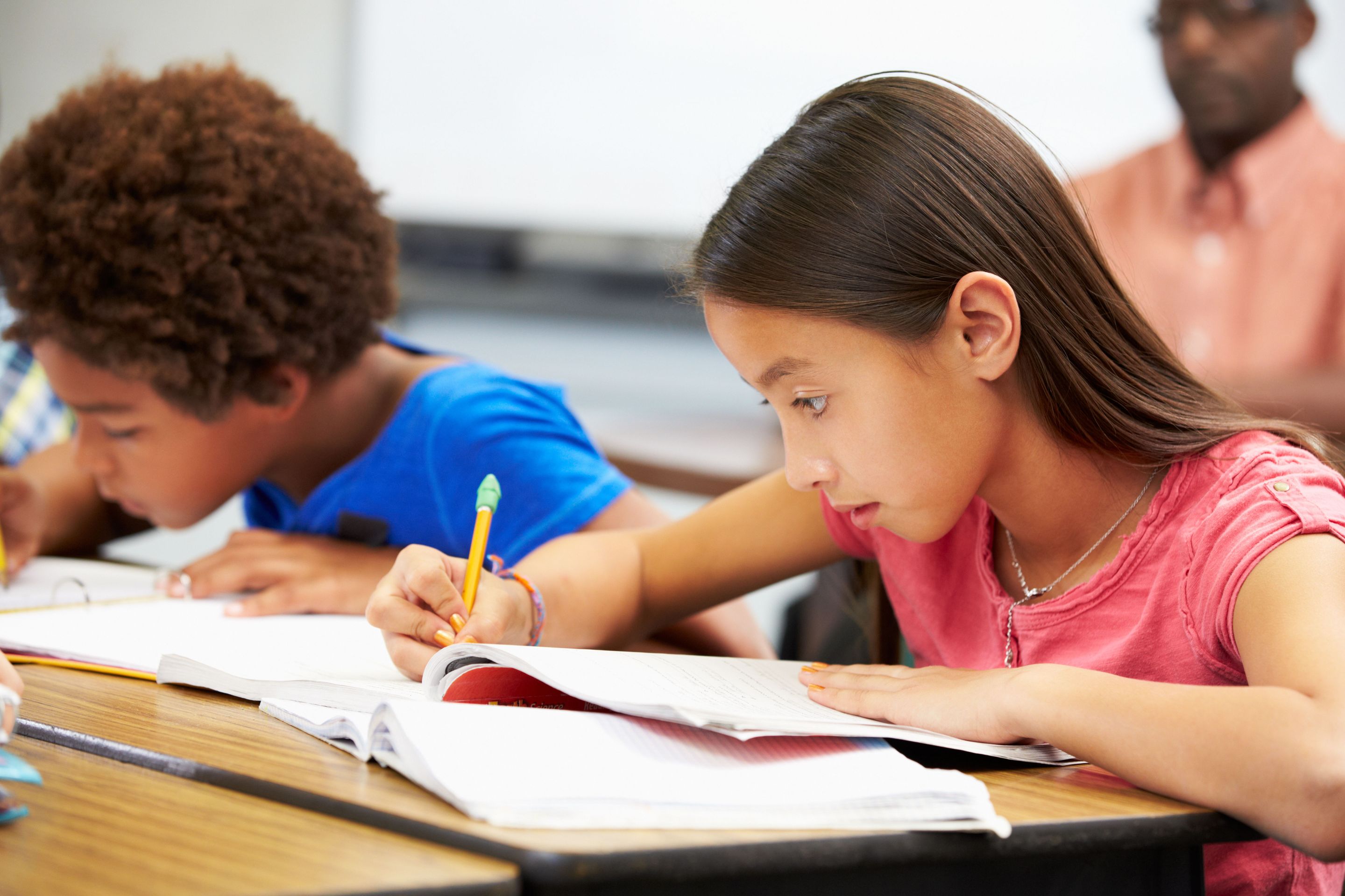 Elementary school students working independently at their desks while a teacher works with another student in the background.