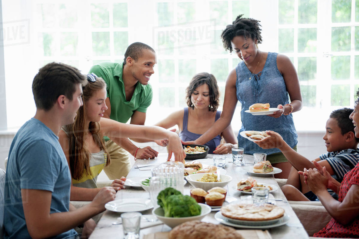 A happy family of different ages sitting around a table, eating a meal and enjoying each other's company.