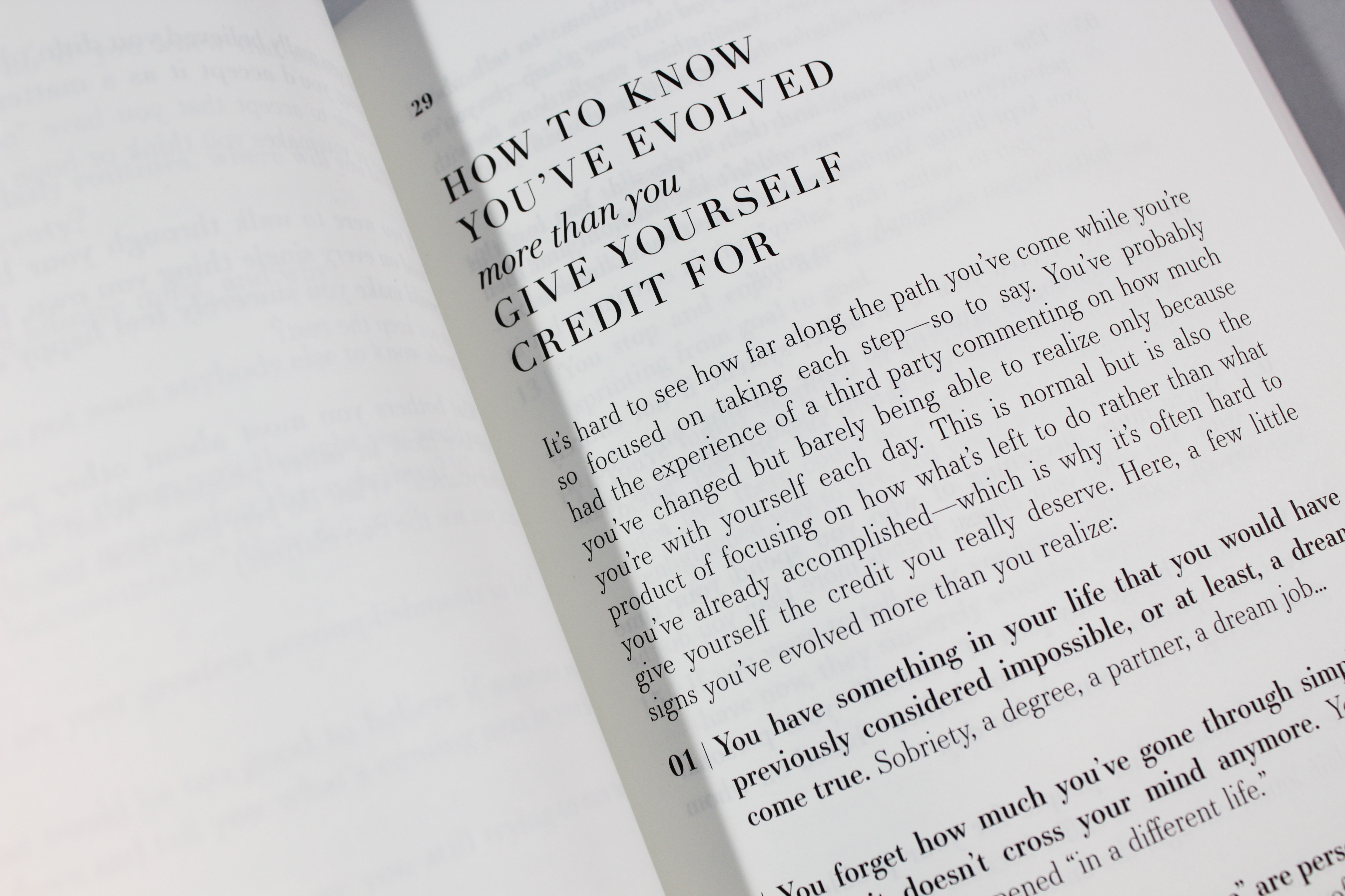 A book opened to a page with a black and white image of a person's hand holding a pen and a magnifying glass over a piece of paper with the words 'It's hard to see how far along the path you've come while you're so focused on taking each step' written on it.