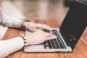 A person wearing a bracelet types on a laptop keyboard while sitting at a desk.