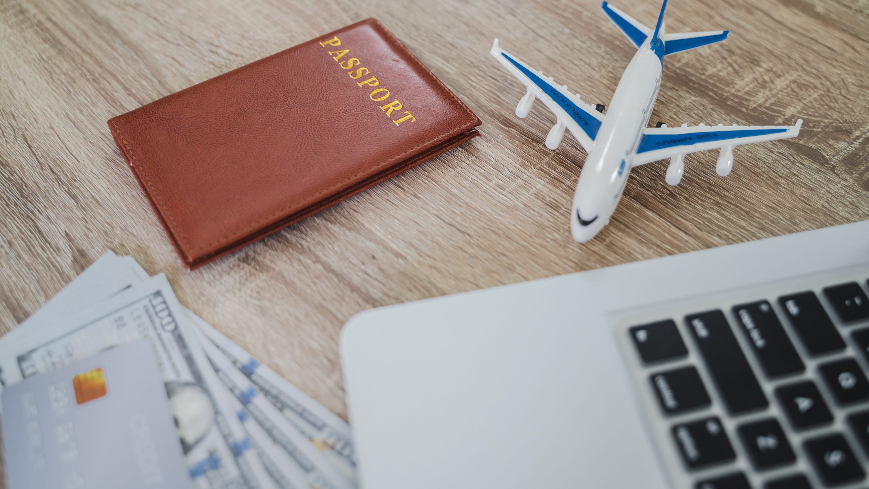 A wooden table with a laptop, a passport, an airplane, and money.