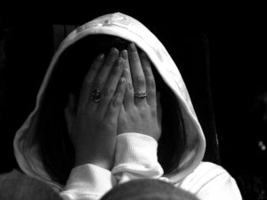 A black and white image of a person wearing a hoodie with their head in their hands.