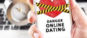 A hand holding a phone with a heart wrapped in caution tape over the screen, symbolizing the dangers of online dating and the need for safe and reputable dating apps.