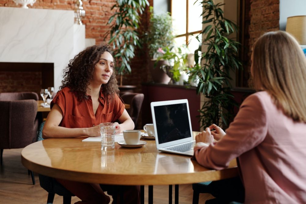 A woman in an orange shirt is talking to another woman in a pink shirt about how to overcome feelings of hopelessness.