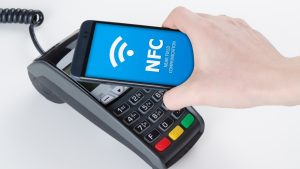 A smartphone is held above a payment terminal to make a contactless payment using the NFC feature.