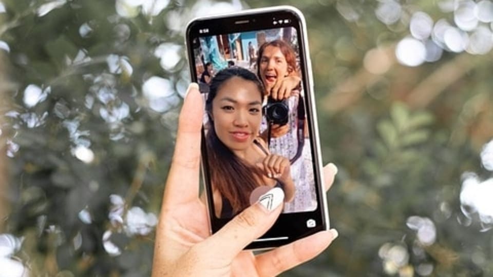 A hand holding a phone with a picture of two women on the screen with text reading 'Repost Instagram Story full screen'.