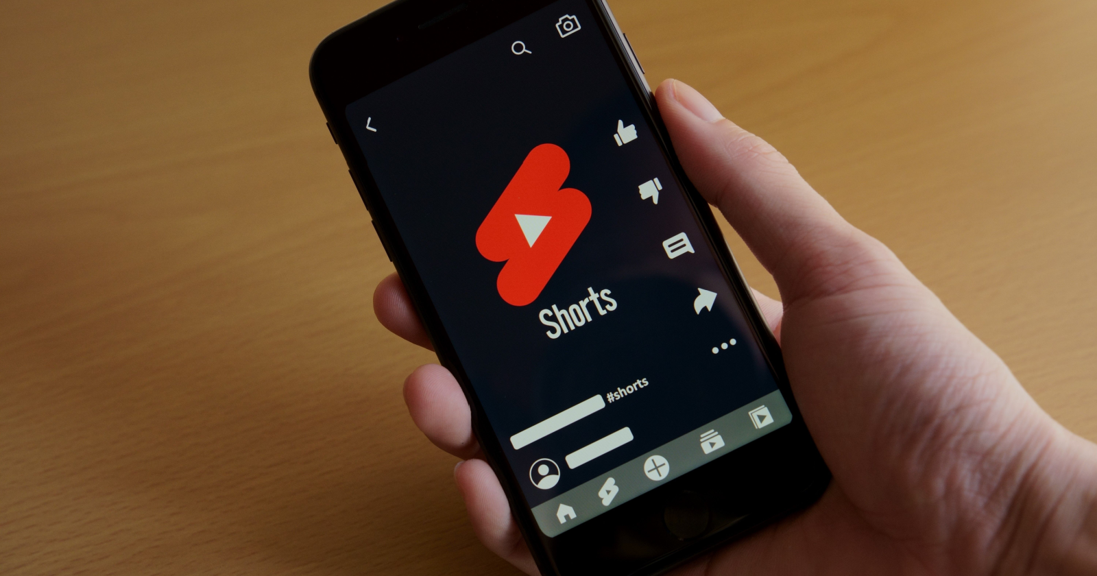 A hand holding a smartphone with the YouTube Shorts app open and "YouTube Shorts monetization requirements" written in the search bar.