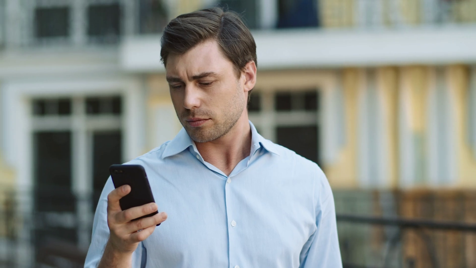 A man in a blue shirt is using the Facebook app on his smartphone while walking down the street.