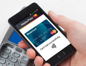 A hand holding a smartphone with the Mastercard app open and a message saying 'Card read successfully' on the screen, and a payment terminal.